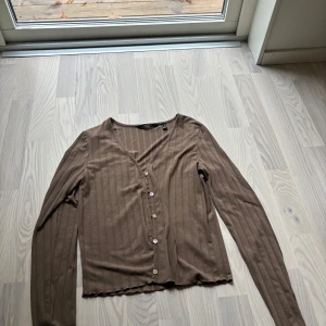 Brun ribbad kofta från Vero Moda - Säljer en brun ribbad kofta från Vero Moda i storlek S. Koftan har v-ringning, långa ärmar och knappar framtill. Materialet är mjukt och stretchigt