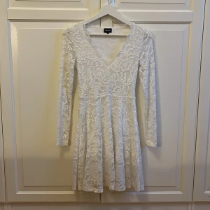 Vit spetsklänning från Bubbleroom XS - Superfin vit kort spetsklänning från Bubbleroom med lång ärm och v-ringning. Klänningen har ett blommigt spetsmönster och är fodrad undertill. Har bara använt en gång på en skolavslutning så den är så gott som ny! Köpt för 750kr 🥰