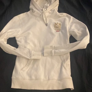 Vit hoodie från Morris  - Säljer en stilren vit hoodie från Morris med snygg broderad logga och brittisk flagga på bröstet. Tröjan har huva med snörning, känguruficka och ribbade muddar. Perfekt för dig som gillar klassisk och clean streetstyle. Stl S