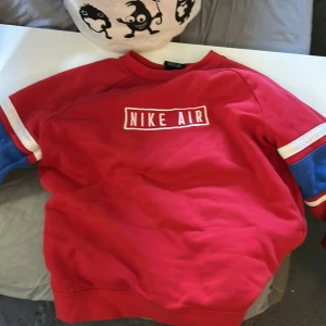 Röd Nike Air sweatshirt XL - Röd Nike Air sweatshirt med tryckt logga på bröstet. Tröjan har blå och vita detaljer på ärmarna och klassisk rund hals. Perfekt för dig som gillar sportig och avslappnad stil.