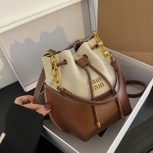 Trendig bucket bag med kedjedetaljer - Snygg bucket bag med coola guldfärgade kedjor och snörning upptill. Väskan har en kombination av beige canvas och detaljer i antingen brunt eller svart skinnimitation. Perfekt storlek för det viktigaste och med justerbar axelrem för skön passform.