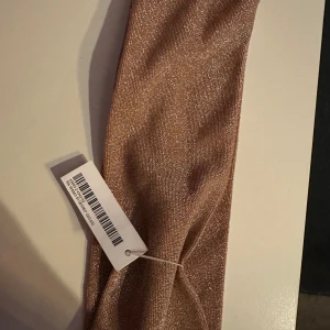Glittrigt champagnefärgat pannband NY! - Snyggt pannband  i champagnefärgad ton med glittrigt tyg som ger en lyxig känsla. Perfekt accessoar för att lyfta din look med lite extra shimmer. Diademet är mjukt och bekvämt att bära och passar till många olika frisyrer.