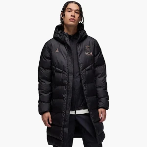 Parka Jacka PSG x Jordan - Lång svart dunjacka med huva från Jordan x PSG. Jackan har broderade loggor på bröstet, hel dragkedja och två sidofickor. Puffig design med horisontella sömmar och sportig vibe. Perfekt för kalla dagar när du vill hålla stilen.