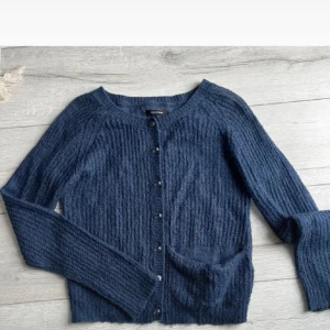 Mörkblå stickad kofta med knappar - Mysig mörkblå stickad kofta från Other Stories med rund halsringning och silvriga knappar framtill. Koftan har lång ärm och en praktisk ficka på ena sidan. Perfekt för lager-på-lager och chill höst- och vinterdagar.