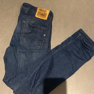 Replay Anbass slim fit jeans blå - Snygga mörkblå Replay Anbass jeans i slim fit-modell. Klassisk femficksdesign med Replay-logga på bakfickan och läderpatch bak i midjan. Jeansen är tillverkade i ett mjukt och slitstarkt bomullstyg med en smal passform som sitter snyggt.