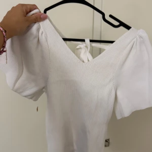 Vit ribbad topp med puffärm och knyt - Superfin vit ribbad topp med v-ringning och puffiga korta ärmar. Toppen har snygg knytning i ryggen som ger en extra detalj. 