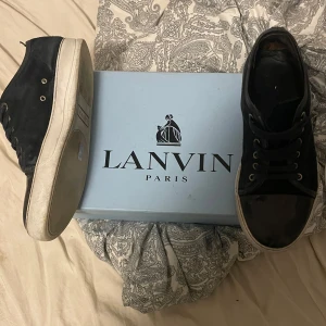 Svarta sneakers från Lanvin Paris - Snygga svarta sneakers från Lanvin Paris med ovandel i mocka och detaljer i blankt skinn vid tån. Skorna har rund tå, snörning med svarta skosnören och vit platt sula. Perfekta för dig som gillar stilrena och lyxiga sneakers med exklusiv känsla.