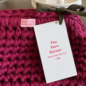 Handgjord vinröd kuvertväska i bomull - Unik handgjord kuvertväska från The Yarn Corner i vinröd färg. Väskan är virkad i tjockt bomullsgarn och har en cool, chunky look. Perfekt för dig som vill sticka ut med en personlig accessoar. Liten etikett med 'hand made' framtill.