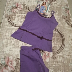 Lila linnetopp med spetsdetaljer - Lila linnetopp från Sueda med smala axelband och dekorativ spetskant i mörkare lila längs urringningen och midjan. Toppen har en liten rosett framtill och är tillverkad i mjuk bomull, perfekt för en avslappnad look.