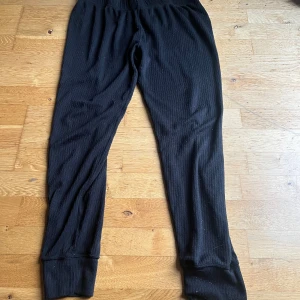 Svarta ribbade byxor från North Bend - Svarta ribbade byxor från North Bend med elastisk midja och smal passform. Mjukt material som känns skönt mot huden, perfekta för chill eller träning. Klassisk look med mudd vid benslut och diskret struktur i tyget.