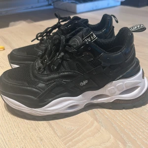 Buffalo svarta chunky sneakers  - Buffalo sneakers i svart med chunky vit och svart sula. Skorna har snörning, mesh och skinnliknande detaljer samt tydlig Buffalo-logga bak och på plösen. Perfekta för dig som gillar en sportig och trendig look med extra höjd. Köpta på footlocker storlek 36 men stora i storleken passar en 37