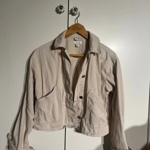 Beige croppad jacka Top Shop - Snygg beige croppad jacka från Top shop med stora fickor framtill och coola knappar. Gott skick!