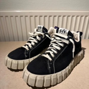 Svarta Eytys Odessa - Säljer ett par svarta Eytys sneakers i storlek 43. Skorna har textilöverdel, tydliga kontrastsömmar och lila hälflik. Perfekta för dig som gillar statement sneakers med unik design. Skorna är sparsamt använda och är i mycket gott skick. Sula är något smuttsig men går lätt att putsa upp!