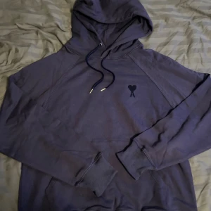 Mörkblå hoodie från Ami Paris - Snygg mörkblå hoodie från Ami Paris med huva och snörning. Tröjan har broderad Ami-logga med hjärta på bröstet och diskret broderad text i nacken. Storleken är L och mitt prs 1300