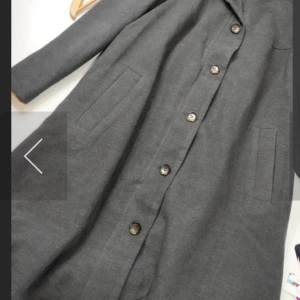 Grå kappa från bpc med knappar - Stilren grå kappa från bpc med snygg krage och stora knappar framtill. Jackan har raka fickor på sidorna och är helfodrad. Perfekt för dig som gillar en klassisk look med modern touch.