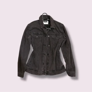 Svart  jeansjacka - Snygg svart jeansjacka  passform och klassisk krage. Jackan har knäppning framtill med svarta knappar och två bröstfickor med lock. Perfekt för dig som gillar en stilren och tidlös look.