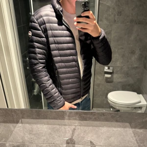 Svart dunjacka från Colmar - Säljer en svart dunjacka från Colmar med horisontella sömmar och hög krage. Jackan har dragkedja framtill, två fickor med dragkedja och en diskret logga på ärmen. Jag är 188cm och bär storlek 48 på bilden. Skriv vid funderingar;)