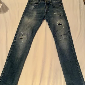 Replay jeans med slitningar, blå, W33 L32 - Snygga blå Replay jeans med slitna detaljer och hål på benen för en cool, avslappnad look. Modellen har klassisk femficksdesign, normal passform och är tillverkad i mjukt denimtyg. Perfekta för dig som gillar streetstyle och vill sticka ut.