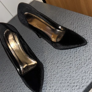 Svarta pumps i sammet med spetsig tå - Snygga svarta pumps i sammet med hög klack och spetsig tå. Skorna har en elegant siluett och en lyxig känsla tack vare det mjuka materialet. Perfekta för dig som vill sticka ut med en klassisk men trendig look.