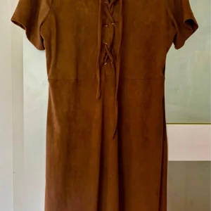 Brun kortärmad klänning med snörning - Snygg brun klänning från Gitten Schmidt Privé i mjuk polyesterblandning. Modellen är kortärmad med cool snörningsdetalj framtill och rak passform. Perfekt för dig som gillar stilrena och trendiga plagg med en twist.