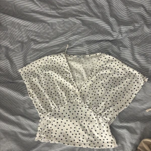 Prickig omlottopp från Zara - Superfin vit omlottopp från Zara med svarta prickar. Toppen har v-ringning, korta ärmar och smockad midja baktill för en snygg passform❤️