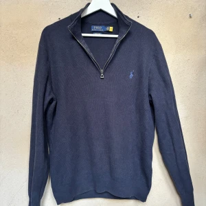 Mörkblå half zip tröja Polo Ralph Lauren - Mörkblå långärmad tröja från Polo Ralph Lauren i mjuk pima bomull. Klassisk modell med half zip-dragkedja och broderad logga på bröstet. Perfekt för lager-på-lager och snygg till både jeans och chinos.