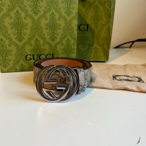 Beige bälte med silvrigt spänne - Snyggt bälte med klassiskt Supreme-mönster i beige och grå toner. Bältet har ett stort, runt spänne i silverfärgad metall.  Tillverkat i canvas med skinn-detaljer. Perfekt accessoar för att lyfta din outfit. Med följer box, påse, kvitto och dustbag (allt på bilderna). Priset kan diskuteras vid snabb affär✅