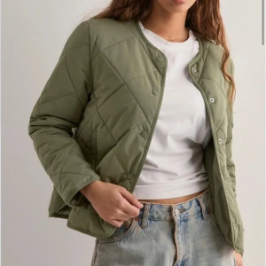 Grön nelly jacka  - Quiltad pufferjacka i olivgrönt med rund halsringning och tryckknappar framtill. Jackan har en boxig passform och diskreta sömmar i rutmönster. Slutsåld på nellys hemsida! Använd fåtal gånger, köpt för 500