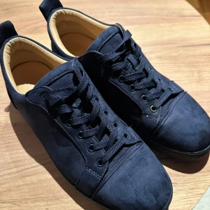 Mörkblå sneakers från Christian Louboutin - Säljer ett par mörkblå sneakers från Christian Louboutin i mocka med klassisk röd sula och broderad logga på hälen. Skorna har rund tå, snörning och en stilren design som sticker ut med den ikoniska röda undersidan.