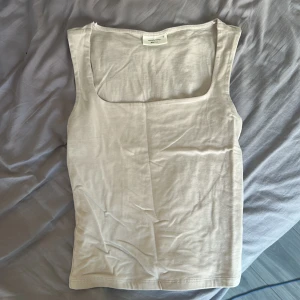 Beige linnetopp från Gina Tricot - Säljer en stilren beige linnetopp från Gina Tricot, basically basics-kollektionen. Toppen har en fyrkantig urringning och är ärmlös, perfekt för en enkel och clean look. Tillverkad i mjuk bomull som känns skön mot huden.