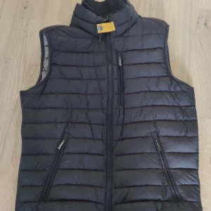  Parajumper väst - Svart quiltad dunväst från Parajumpers i superlätt material. Västen har ståkrage med gul detalj, tre dragkedjefickor framtill och horisontella sömmar. Perfekt för lager-på-lager och snygg till både hoodie och t-shirt.