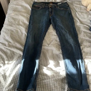 Blå Lee Luke jeans W32 L32 - Säljer ett par klassiska blå Lee Luke jeans i storlek W32 L32. Jeansen har en snygg tvätt, raka ben och detaljerade sömmar med Lee-logga på bakfickan. Perfekta för dig som gillar en tidlös och clean look.