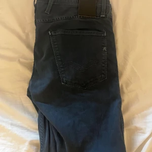 Replay svarta jeansbyxor W31 L34 - Svarta jeansbyxor från Replay med klassisk femficksdesign och diskret logga på bakfickan. Byxorna har raka ben och är tillverkade i mjukt bomullsmaterial med en mörk tvätt. Perfekta för dig som gillar stilrena och bekväma jeans.