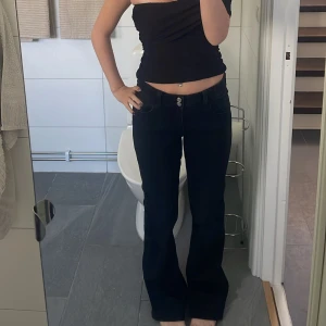 Svarta bootcut jeans med hög midja - Snygga svarta jeans med bootcut-modell och hög midja. Jeansen har klassiska fickor fram och bak, bälteshällor och stängs med dubbla knappar och dragkedja. Perfekta för dig som gillar en tidlös och trendig look.