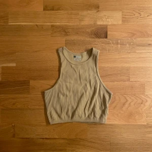 Beige ribbad linnetopp  - Säljer en beige ribbad linnetopp. Toppen är ärmlös med hög halsringning och croppad passform, perfekt för en avslappnad och trendig look. Tillverkad i mjuk bomull med stretch för extra komfort.
