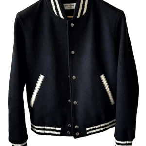 Svart bomberjacka från Saint Laurent nyskick - Svart bomberjacka från Saint Laurent med vita ränder på krage, ärmslut och midja. Jackan har tryckknappar framtill, två fickor med vita detaljer och stor broderad Saint Laurent-logga på ryggen. Tillverkad i ullblandning för en lyxig känsla.