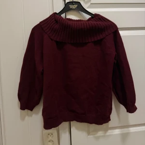 Vinröd offshoulder stickad tröja - Vinröd stickad tröja med bred ribbad krage som kan bäras offshoulder. Tröjan har långa ärmar och en loose passform, perfekt för höst och vinter. Mjuk och skön, passar till jeans eller kjol för en chill look.
