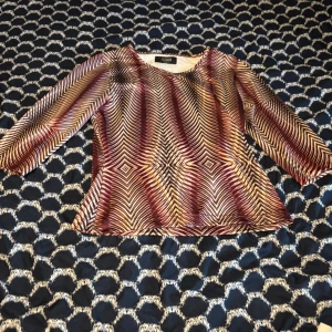 Mönstrad blus från Jasmin i brunt och vinrött - Säljer en unik blus från Jasmin med grafiskt mönster i bruna, beige och vinröda toner. Blusen har trekvartsärm och rund halsringning. Materialet är mjukt och följsamt, perfekt för dig som vill sticka ut med coola mönster och färger.