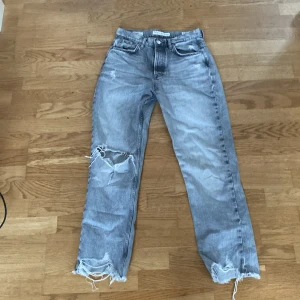 Grå straight jeans  - Gråa straight fit jeans med slitna detaljer och trasiga knän. Klassisk femficksmodell med råa benslut och en gullig design på bakfickan. Jeansen har en avslappnad passform och är tillverkade i denim av bomull.