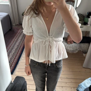 Vit blus med knyt från Gina Tricot - Supersöt vit blus från Gina Tricot i storlek XS. Den har puffiga korta ärmar, v-ringning och knyt i midjan med två rossetter. Blusen är tillverkad i ett strukturerat bomullstyg och har volangkant vid ärmslut och midja. Perfekt för vår och sommar!