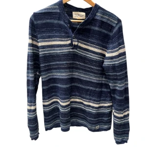 Randig stickad tröja från Ralph Lauren - Säljer en stickad tröja från Denim & Supply Ralph Lauren i marinblått och vitt med randigt mönster. Tröjan har lång ärm, knappar vid halsen och en avslappnad passform. Perfekt för dig som gillar en chill och klassisk stil.