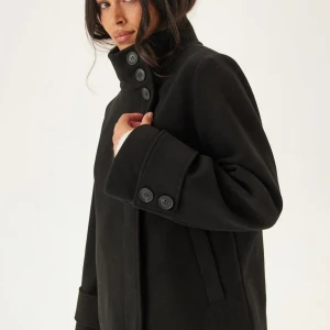 Svart skepparkavaj med hög krage - Jackan har en rak passform och är tillverkad i ett tjockare ullmaterial som håller värmen. Perfekt för kyliga dagar och ger en cool, klassisk look🥰Kappan är helt slutsåld i alla storlekar på hemsidan!