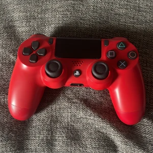 PlayStation DualShock 4 Wireless Controller (Röd) - Snygg röd DualShock 4 trådlös handkontroll till PlayStation 4. Kontrollen är i gott skick med minimalt slitage och alla knappar och spakar ser ut att fungera som de ska. Perfekt för gaming eller som extra kontroll till din PS4.