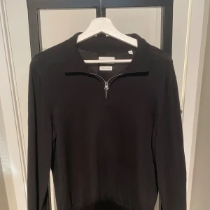 Svart half zip-tröja These Glory Days - Svart långärmad tröja från These Glory Days i mjuk bomull. Klassisk krage och snygg half zip-dragkedja framtill. Perfekt för dig som gillar stilren och enkel design med en modern touch.