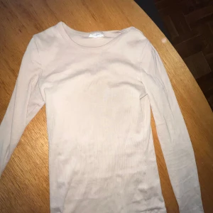 Beige långärmad tröja från Tricot - En enkel och stilren beige långärmad tröja från Tricot, perfekt för layering. Modellen är ribbad och har en rund halsringning. Mjuk och skön bomullskvalitet som passar dig som gillar basic-plagg med clean look.