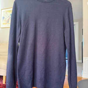 Mörkblå stickad tröja i klassisk modell - En stilren mörkblå stickad tröja med rund halsringning och långa ärmar. Tröjan har en enkel och tidlös design med ribbade muddar vid ärmslut och nederkant. Perfekt för lager-på-lager och passar till det mesta i garderoben.