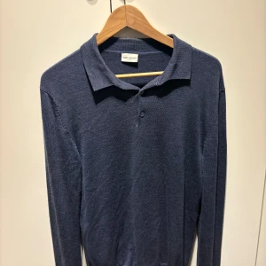 Mörkblå pikétröja från John Henric storlek S - Snygg mörkblå pikétröja från John Henric med klassisk krage och två knappar framtill. Tröjan är långärmad och tillverkad i mjuk bomull, perfekt för en stilren och avslappnad look.