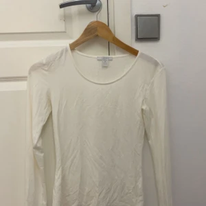 Vit långärmad topp - En enkel och stilren vit långärmad topp. Modellen har rund halsringning och är figurnära i passformen. Perfekt att matcha med jeans eller kjol för en clean look.