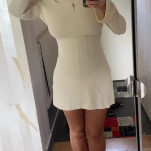 Vit ribbad kort stickad klänning - Supersöt kort klänning med ribbat mönster och lång ärm. Klänningen har öppen rygg med knytband och lätt utsvängda ärmar. Kom ihåg att andra bilden så sträcker jag på armarna på bilden så den blir kortare men annars är den längre men den åker upp när man sträcker på sig (som alla klänningar). Den är mycket stretchig så den är S men passar M oxå och kanske L. Jag skulle säga att den är mer krämvit än vit💕den är liiite genomskinlig som man kan se på andra bilden (där har jag svarta underkläder) ✨