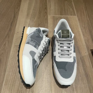 Valentino Garavani Rockrunner sneakers - Snygga Valentino Garavani Rockrunner sneakers i vitt och grått med meshpaneler och detaljer i mocka och skinn. Skorna har en beige sula med svarta räfflor och klassisk snörning. Kommer med originalkartong och röd dustbag.